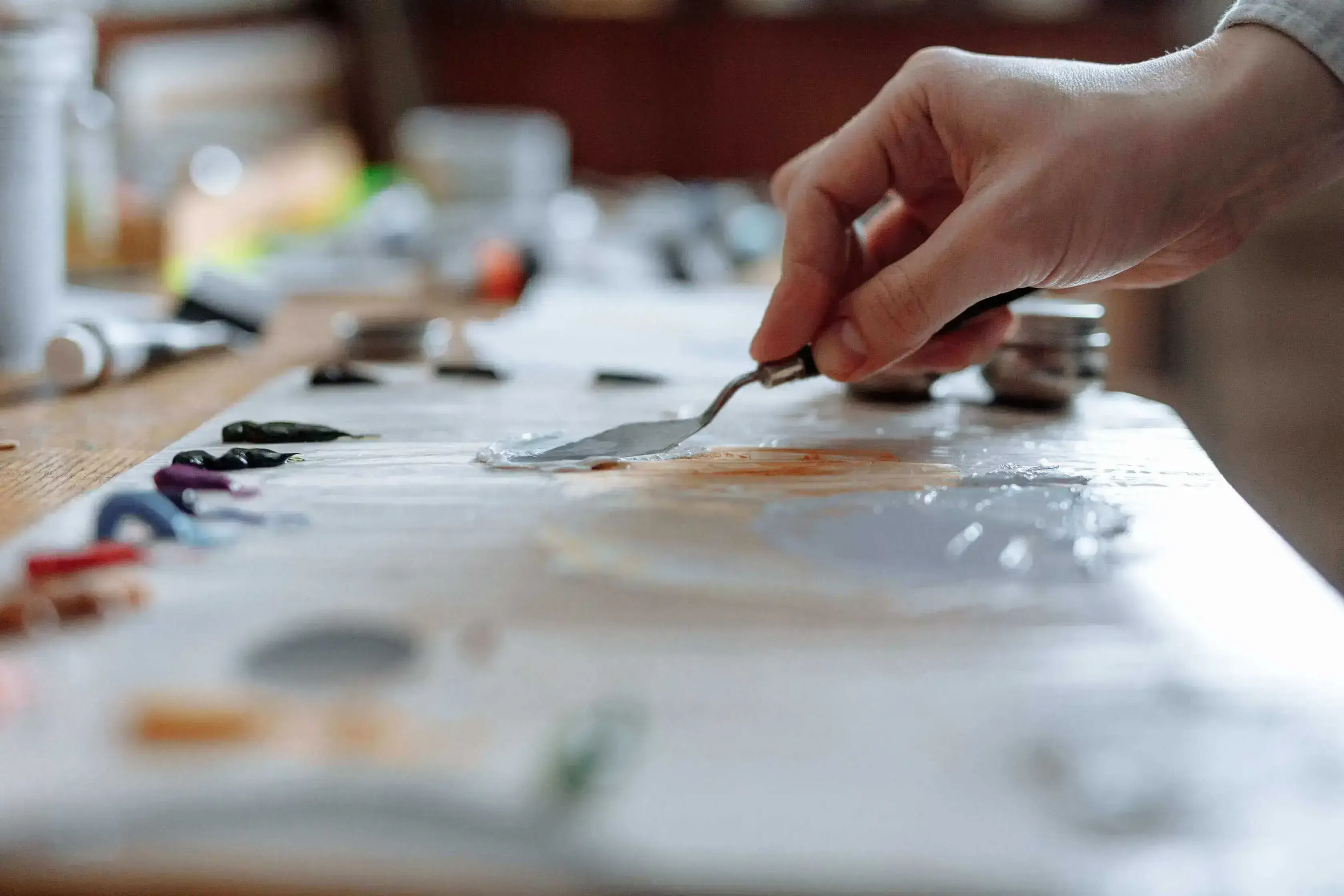 A hand applying oil paint using a palette knife using many different colours.