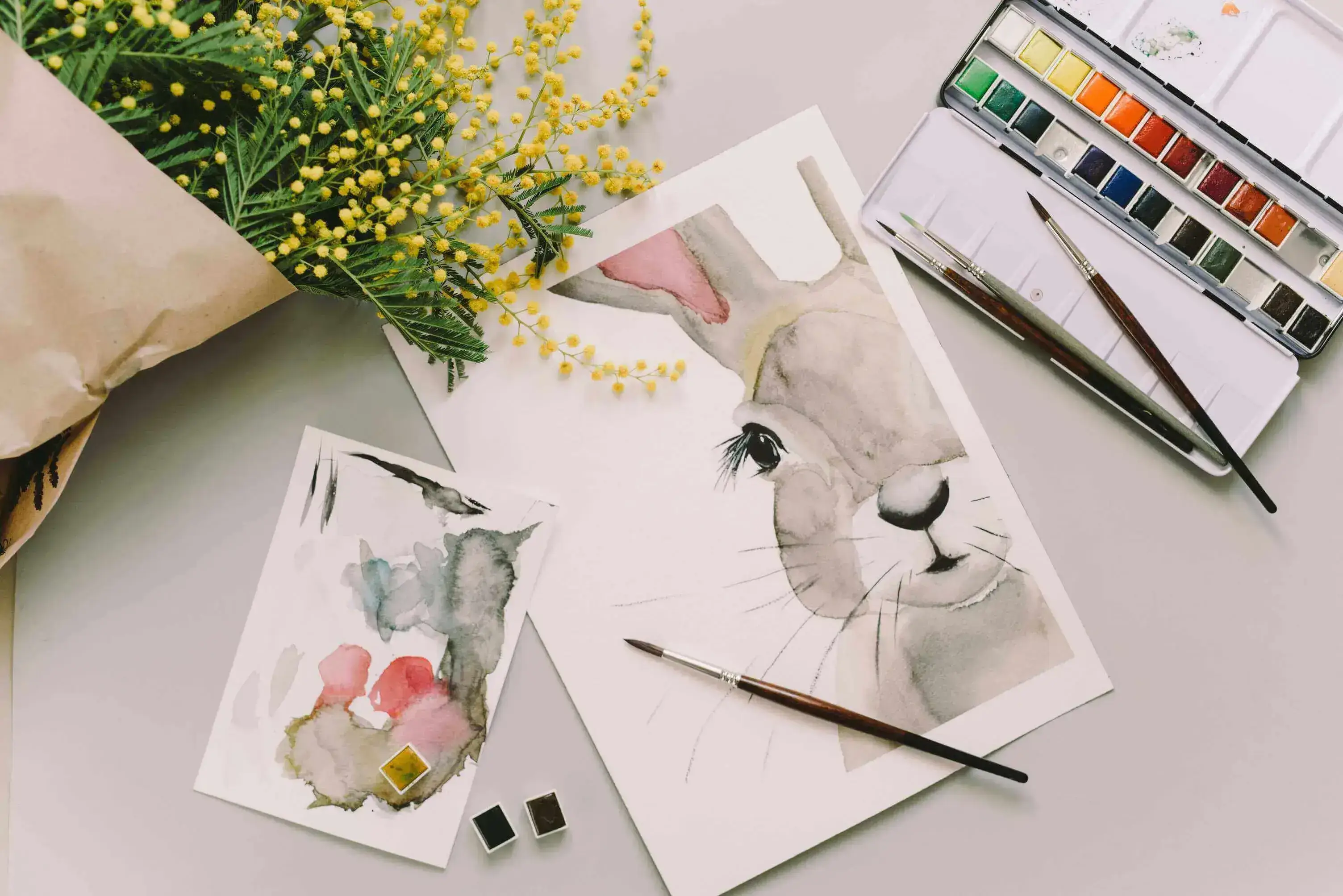 Watercolour painting of a grey rabbit next to flowers.